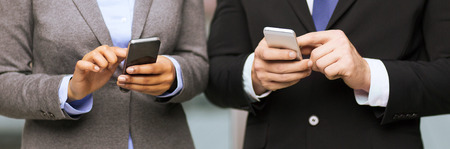 business, technology, internet and office concept - businessman and businesswoman with smartphones in officeの写真素材