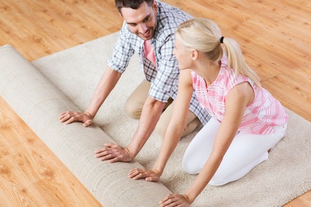 happy couple unrolling carpet or rug on floor at homeの写真素材