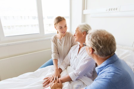 medicine, support, family health care and people concept - happy senior man and young woman visiting and cheering her grandmother lying in bed at hospital wardの写真素材