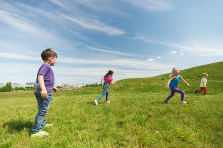summer, childhood, leisure and people concept - group of happy kids playing tag game and running on green field outdoorsの写真素材