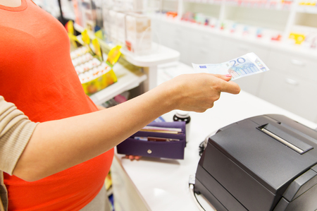 medicine, pharmaceutics, health care and people concept - close up of pregnant woman giving money and buying medication at cash register in drugstoreの写真素材