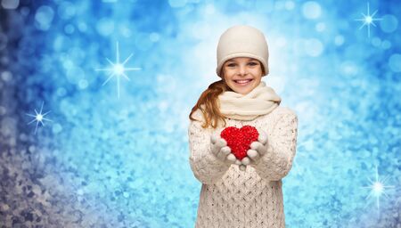 christmas, winter, holidays and childhood concept - smiling teenage girl in winter clothes with small red heart over blue glitter or lights backgroundの写真素材