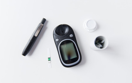 medicine, diabetes and health care concept - close up of glucometer with stick and blood sugar test stripes container on tableの写真素材