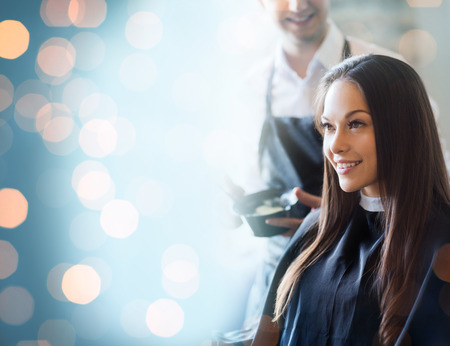 beauty and people concept - happy young woman with hairdresser coloring hair at salonの写真素材