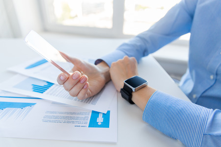 business, technology and people concept - close up of woman hand holding and showing transparent smart phone and watch at officeの写真素材