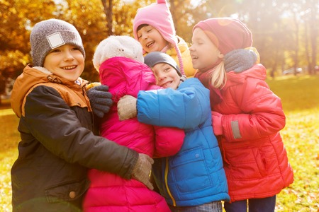 childhood, leisure, friendship and people concept - group of happy kids hugging in autumn park