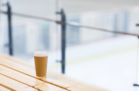 hot drink, winter and leisure concept - close up of coffee cup on wooden bench at skating rink