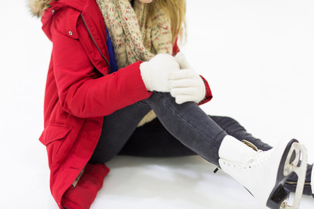 people, sport, trauma, pain and leisure concept - close up of young woman fell down on skating rink with knee injury holding to her legの写真素材