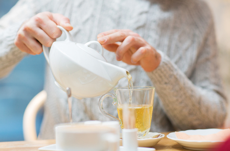 people, leisure and drinks concept - close up of man pouring tea from pot to cup at cafeの写真素材