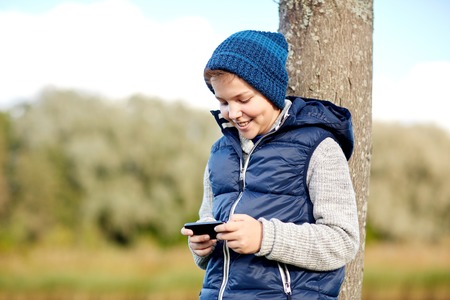 people, children and technology concept - happy teenage boy playing game or texting message on smartphone outdoorsの写真素材