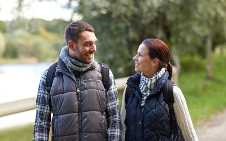adventure, travel, tourism, hike and people concept - happy family couple walking with backpacks in woodsの写真素材