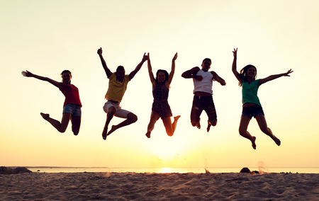 friendship, summer vacation, holidays, party and people concept - group of smiling friends dancing and jumping on beachの写真素材