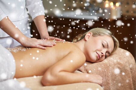 people, beauty, spa, winter and relaxation concept - close up of beautiful young woman lying with closed eyes and having salt back massage in spa with snow effectの写真素材