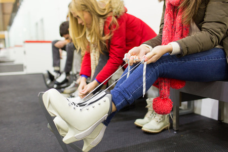 people, winter sport and leisure concept - close up of woman wearing and lacing skates on skating rinkの写真素材