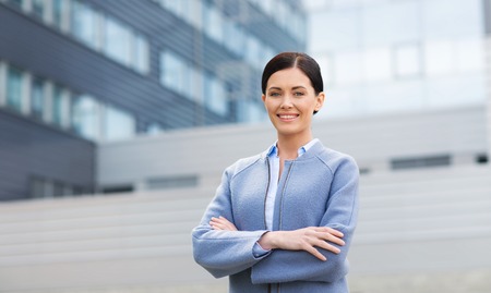 business and people concept - young smiling businesswoman over office buildingの写真素材