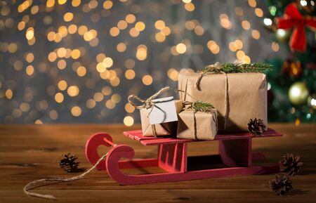 holidays, presents, new year and celebration concept - close up of gift boxes with blank note on red wooden sleigh over christmas tree and lights backgroundの写真素材