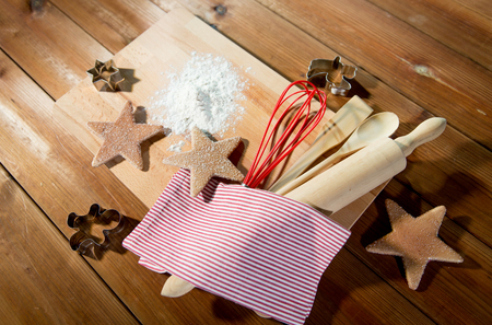 baking, cooking, christmas and food concept - close up of gingerbread cookies, molds with flour and kitchenware set on wooden cutting board at home kitchen from topの写真素材