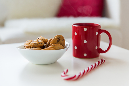 christmas, holidays, winter and celebration concept - close up of oat cookies, sugar cane candy and red cup on table at homeの写真素材