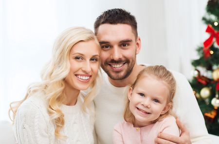family, christmas, holidays and people concept - happy mother, father and little daughter sitting on sofa at homeの写真素材
