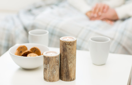 christmas, winter, holidays and concept - close up of candles, cookies and tea cups on table over family couple on backgroundの写真素材
