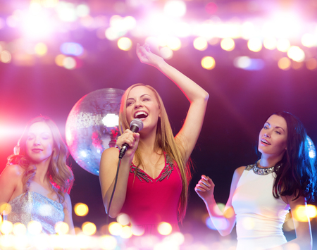 party, holidays, nightlife, entertainment and people concept - concept - happy women with microphone singing karaoke and dancing at night clubの写真素材