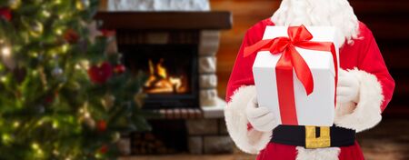 christmas, holidays and people concept - close up of santa claus with gift box over living room with fireplace and christmas tree backgroundの写真素材