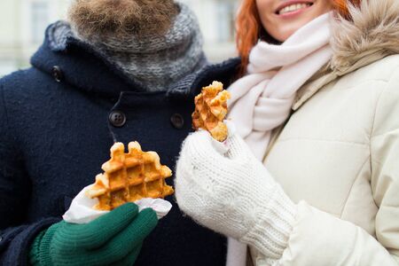 holidays, winter, christmas and people concept - close up of happy couple eating waffles outdoorsの写真素材