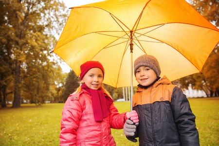 childhood, friendship, season, weather and people concept - happy little boy and girl with umbrella in autumn parkの写真素材