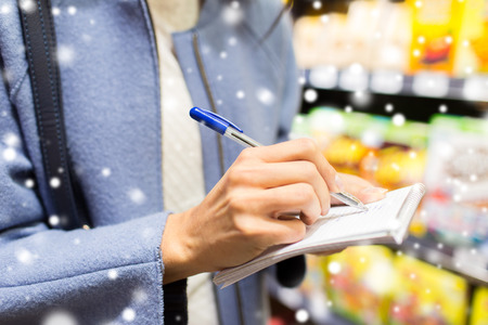 sale, shopping, consumerism and people concept - close up of young woman with pen taking notes to notebook in market over snow effectの写真素材