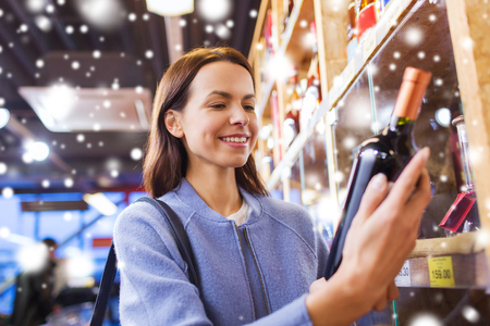 sale, shopping, holidays, consumerism and people concept - happy young woman choosing and buying wine in market over snow effectの写真素材