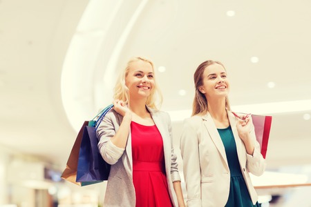 sale, consumerism and people concept - happy young women with shopping bags in mallの写真素材