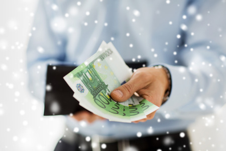 people, business, finances and money concept - close up of businessman hands holding open wallet with euro cash over snow effectの写真素材
