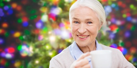 holidays, age, drink and people concept - happy smiling senior woman with cup of tea or coffee over...