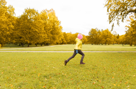 season, childhood, activity, motion and happiness and people concept - happy little girl running in autumn parkの写真素材