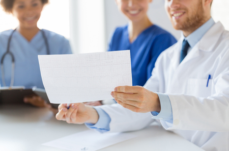 hospital, cardiology, people and medicine concept - close up of happy doctors looking at cardiogram at medical officeの写真素材