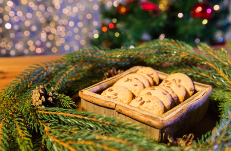 christmas, holidays, food and baking concept - close up of natural green fir christmas wreath and oat cookies in wooden box on table over lightsの写真素材