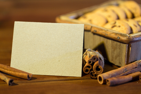 baking, culinary, holidays and food concept - close up of blank greeting card with oat cookies in wooden box and cinnamon on tableの写真素材