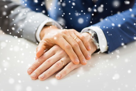 people, homosexuality, same-sex marriage and love concept - close up of happy male gay couple hands with wedding rings on over snow effectの写真素材