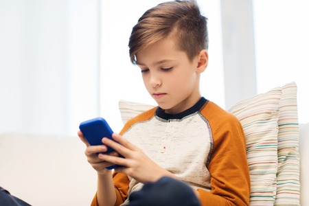 leisure, children, technology, internet addiction and people concept - boy with smartphone texting message or playing game at homeの写真素材