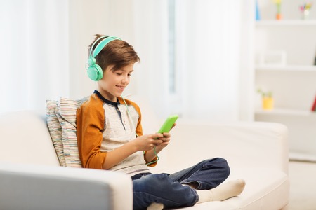 leisure, children, technology and people concept - smiling boy with smartphone and headphones listening to music or playing game at homeの写真素材