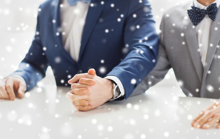 people, homosexuality, same-sex marriage and love concept - close up of happy male gay couple holding hands on wedding over snow effectの写真素材