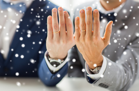 people, celebration, homosexuality, same-sex marriage and love concept - close up of male gay couple with wedding rings on putting hand on shoulder over snow effectの写真素材