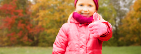 autumn, childhood, season, gesture and people concept - close up of happy little girl showing thumbs up outdoors over natural backgroundの写真素材
