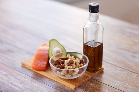healthy eating, diet and culinary concept - close up of salmon fillets, avocado, olive oil bottle and nuts in glass bowl on tableの写真素材