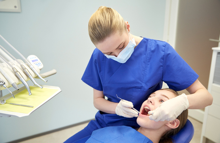people, medicine, stomatology and health care concept - happy female dentist with mirror and probe checking patient girl teeth up at dental clinic officeの写真素材