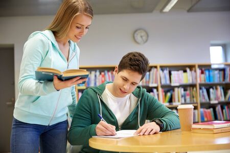 people, knowledge, education and school concept - happy students with book preparing to exams in libraryの写真素材
