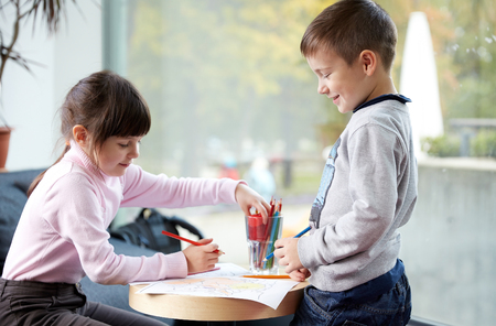 childhood, leisure, friendship and people concept - happy little girl and boy drawing and coloring picture with pencils at homeの写真素材