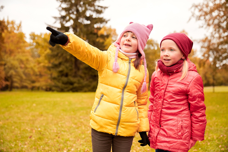 autumn, childhood, leisure, gesture and people concept - happy little girls pointing finger in park outdoorsの写真素材
