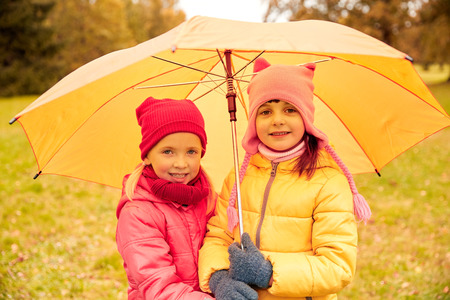 childhood, friendship, season, weather and people concept - happy little girls with umbrella in autumn parkの写真素材
