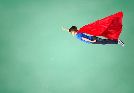 freedom, childhood, education, movement and people concept - boy in red superhero cape and mask flying in air over green school chalk board backgroundの写真素材
